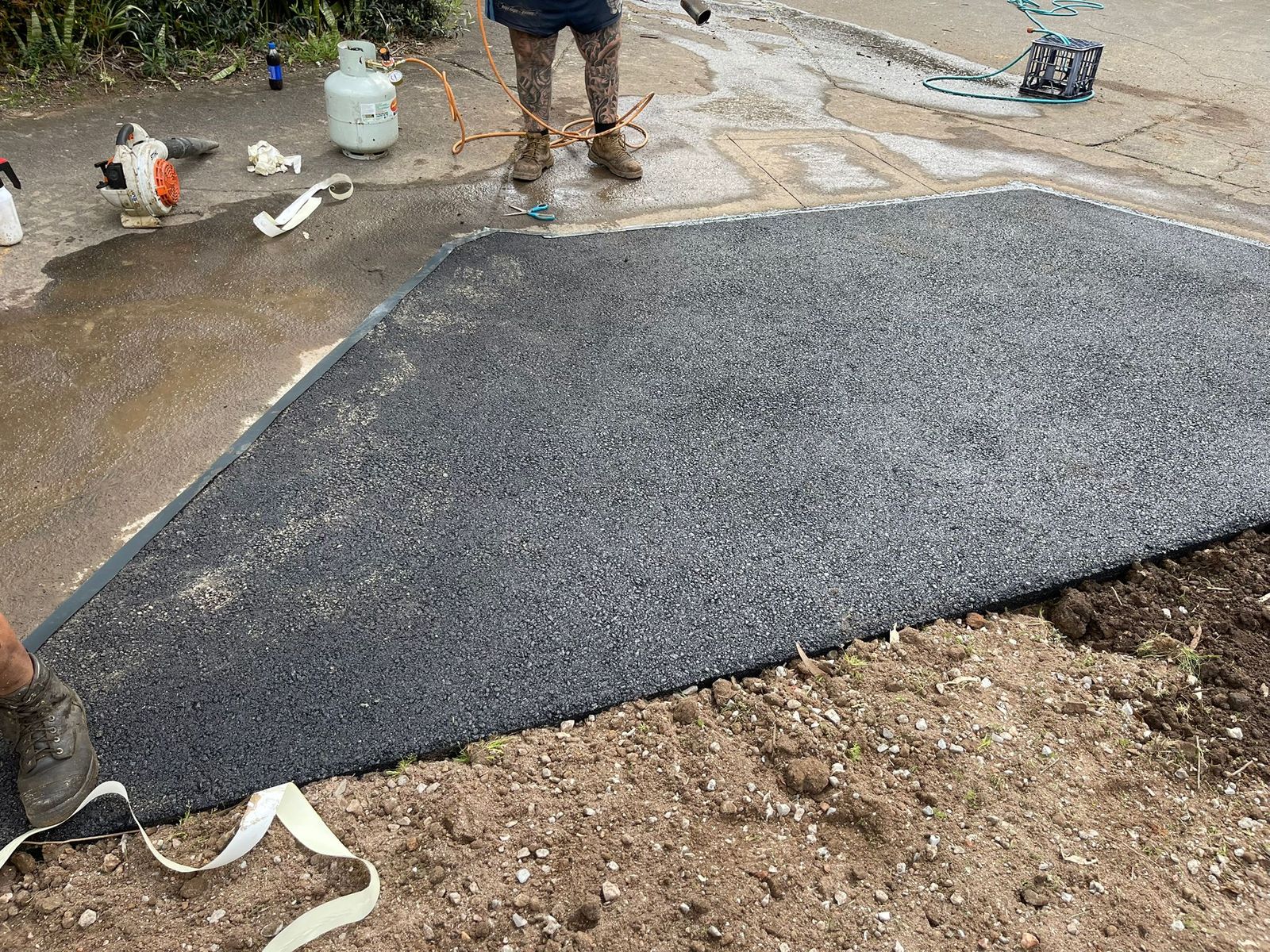 New asphalt surface patch freshly laid beside an existing concrete area