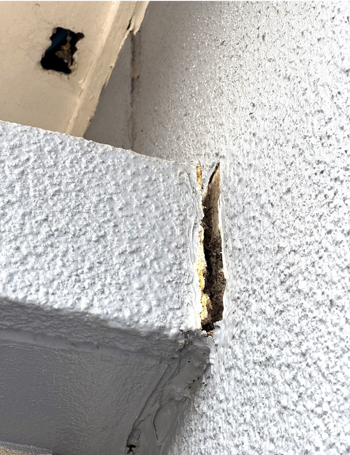 Close-up of a gap and deteriorated material where an awning slab edge meets a rendered wall