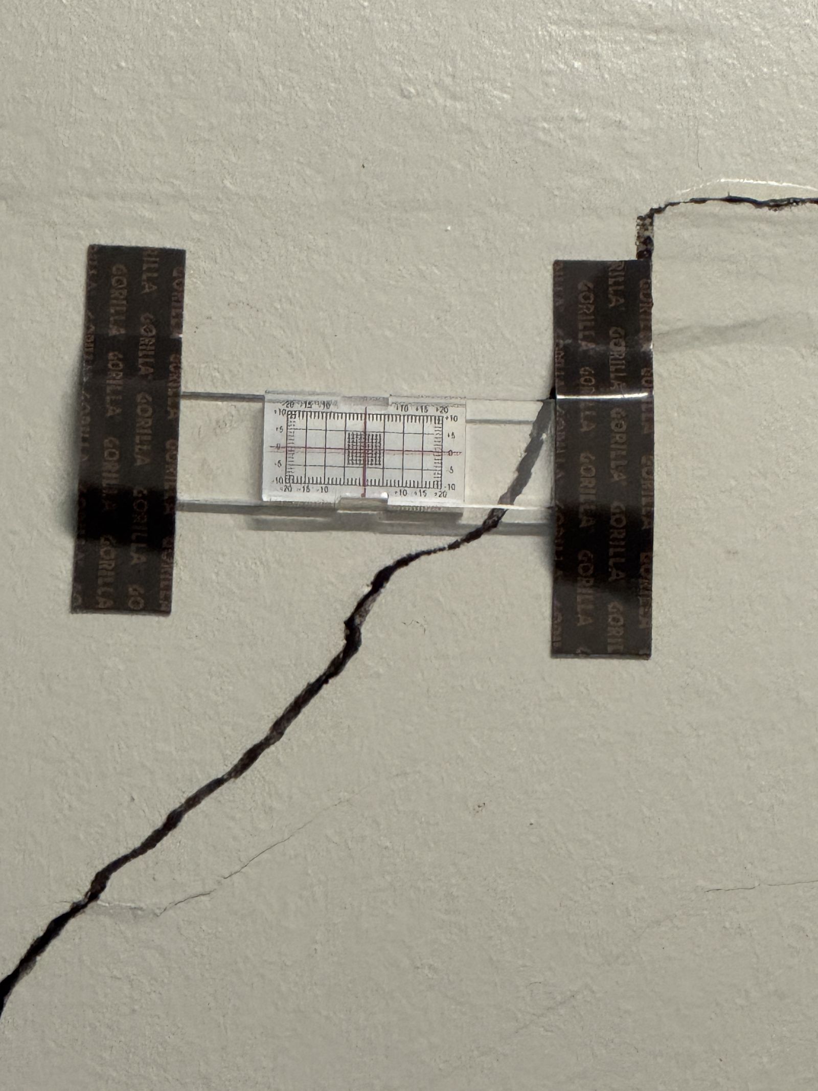 Crack monitoring gauge taped across a diagonal crack in a painted internal wall